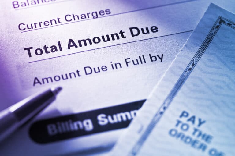 Close-up of a bill with the text "Total Amount Due" and "Amount Due in Full by," next to a pen. A separate document with partial text "Pay to the Order of" is also visible.