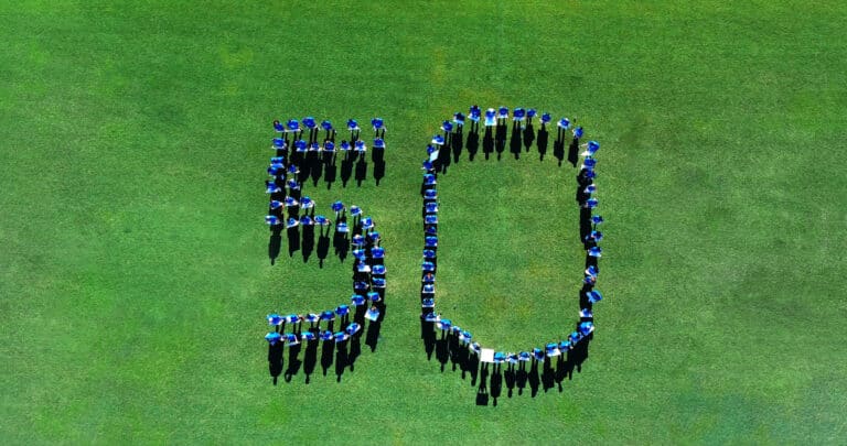 A group of people wearing blue shirts stand on grass, forming the number 50.