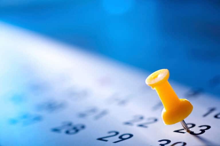 Close-up of a yellow push pin on a calendar page, highlighting the number 23.