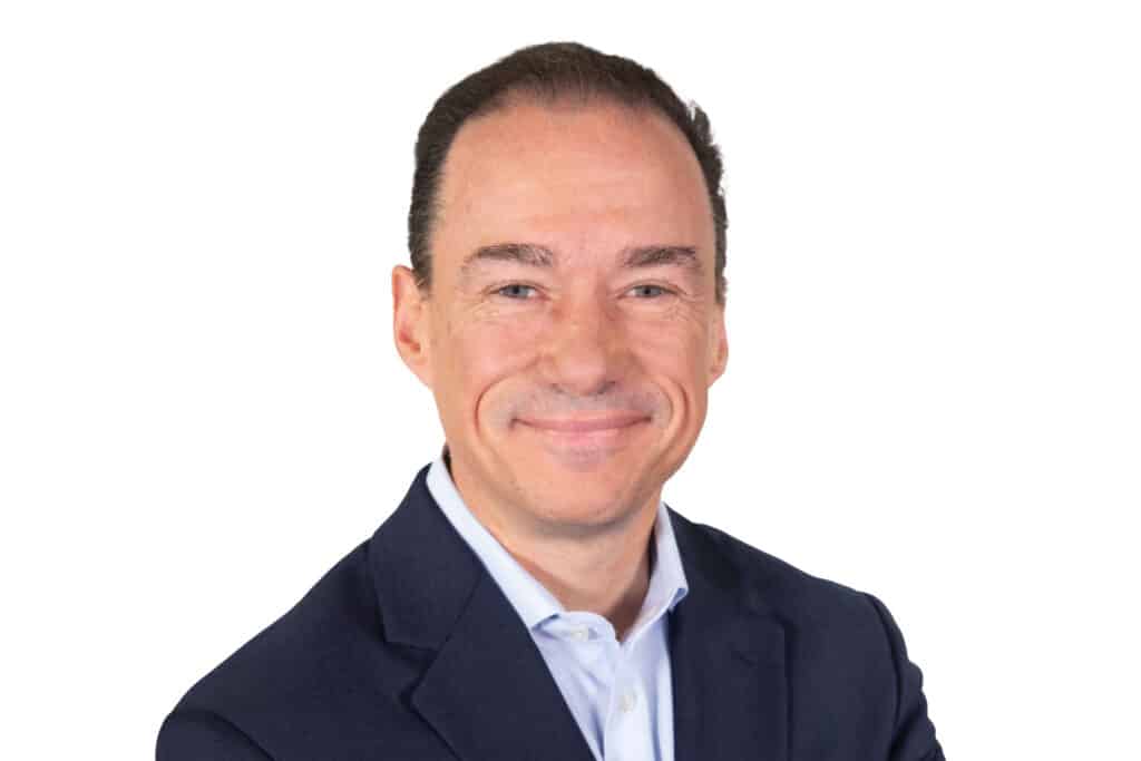 A man in a suit smiling against a white background.