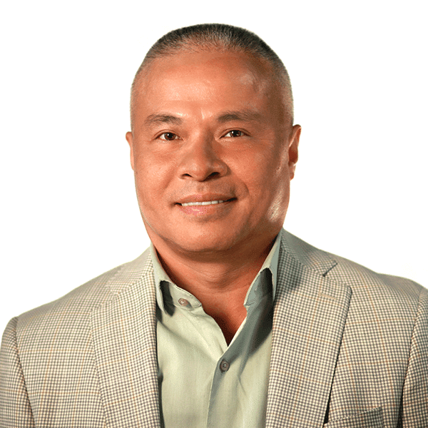 A person with short hair in a light gray suit and green shirt smiles against a white background.