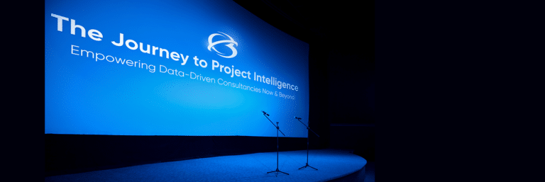 Blue presentation screen with the text "The Journey to Project Intelligence: Empowering Data-Driven Consultants Now & Beyond," and two microphones on stage.