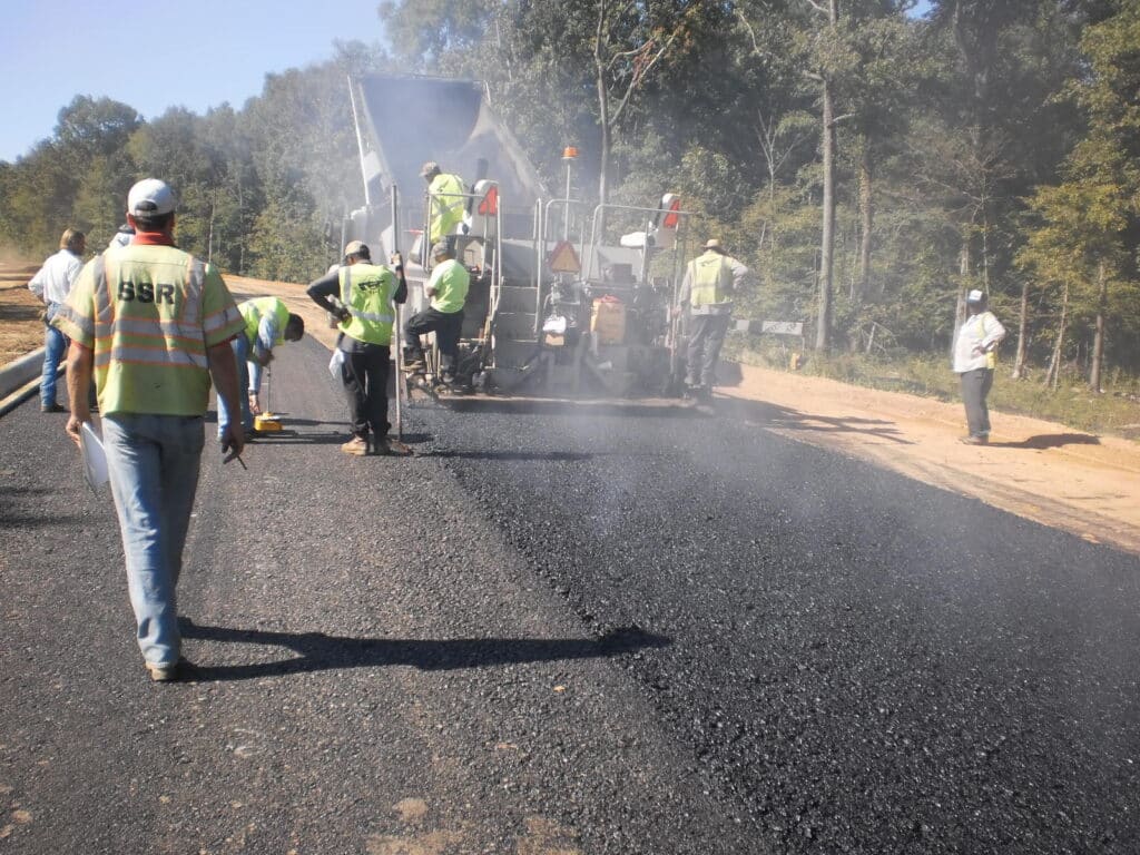 Workers paving a road with asphalt using heavy machinery on a sunny day.