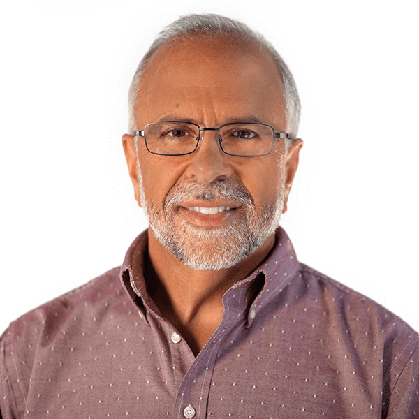 A man with glasses and a beard wearing a dotted shirt smiles against a plain white background.