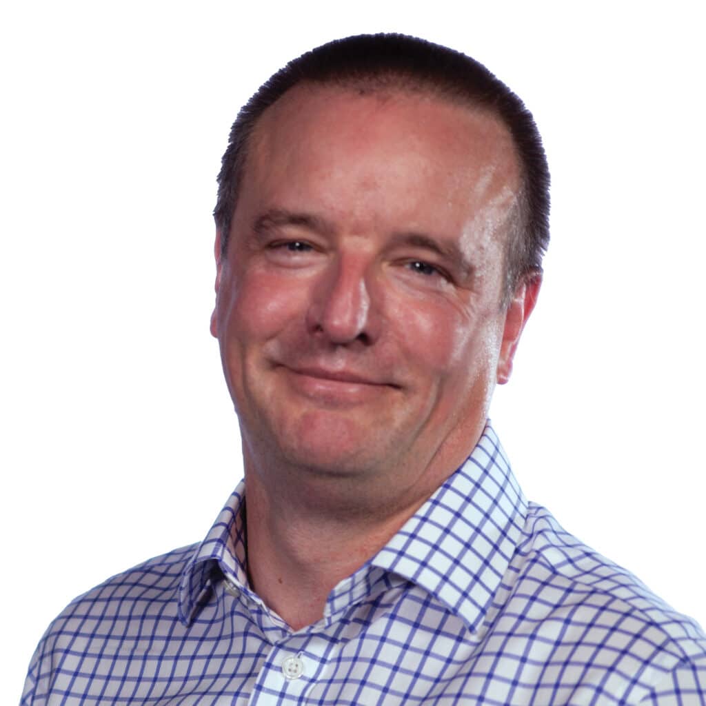 A man with short hair wearing a checkered shirt smiles slightly against a plain white background.