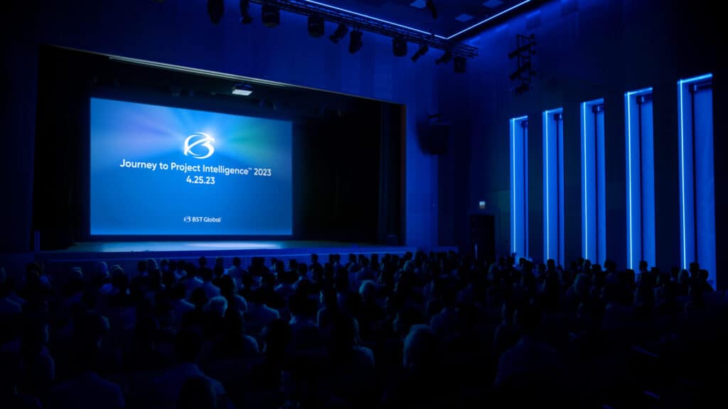 A dimly lit auditorium with a large screen displaying "Journey to Project Intelligence 2023, 4.5.23, KST Global" to an audience.