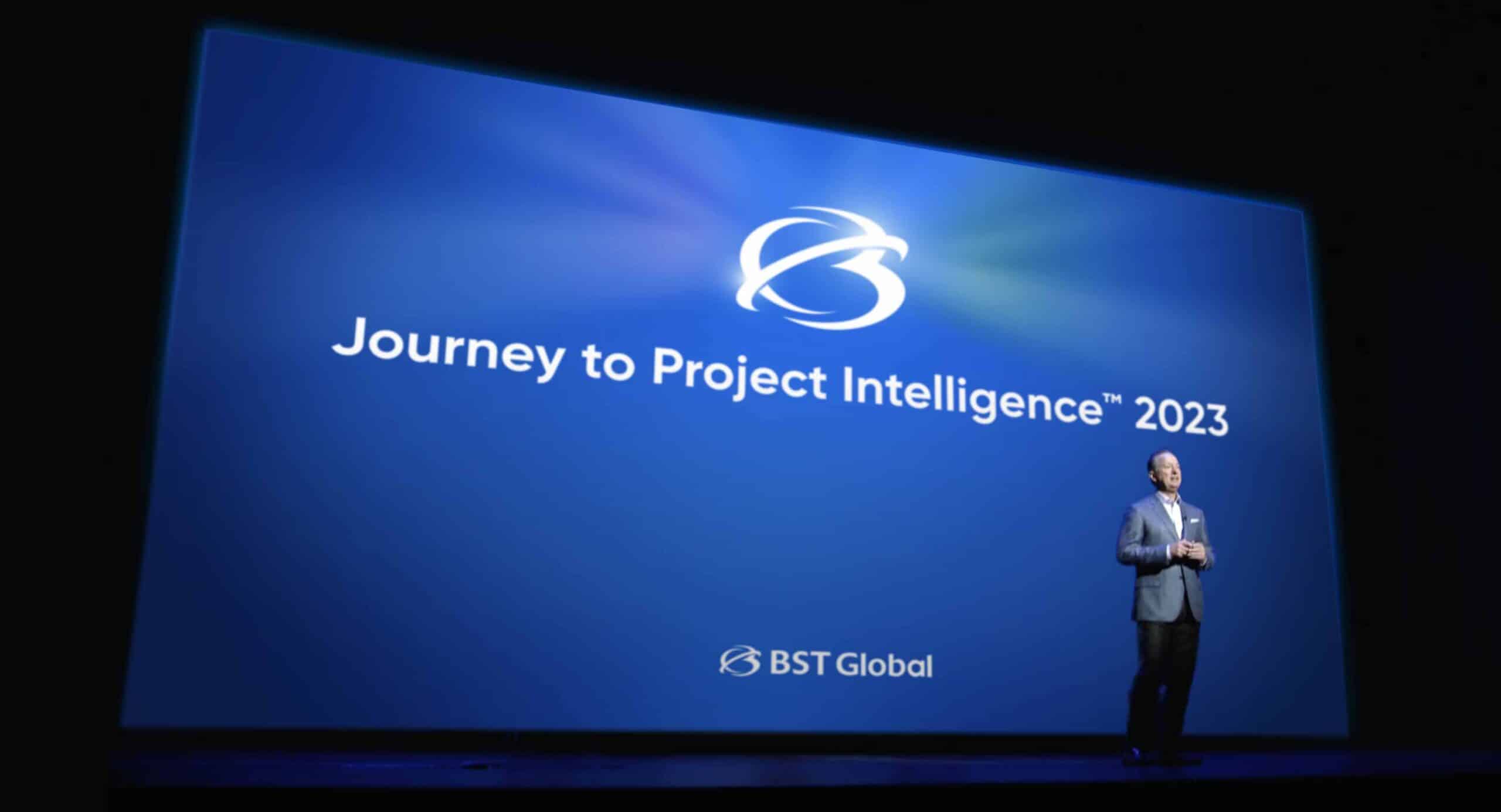 Man standing on stage next to a large screen displaying "Journey to Project Intelligence™ 2023" with the BST Global logo.