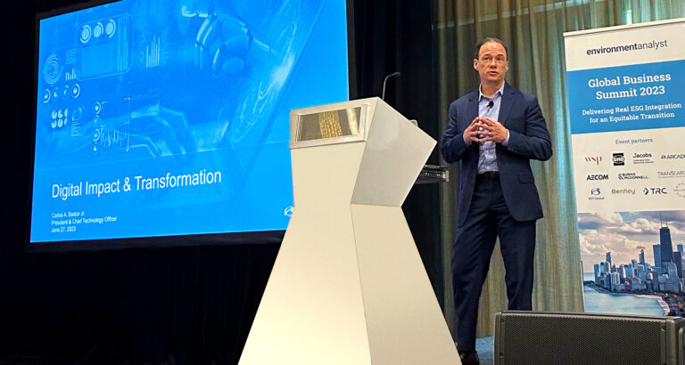 A man presents at the Global Business Summit 2023, standing near a podium and a screen displaying "Digital Impact & Transformation.