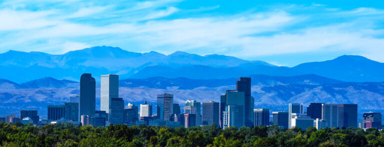 City skyline with tall buildings and mountains in the background under a blue sky.