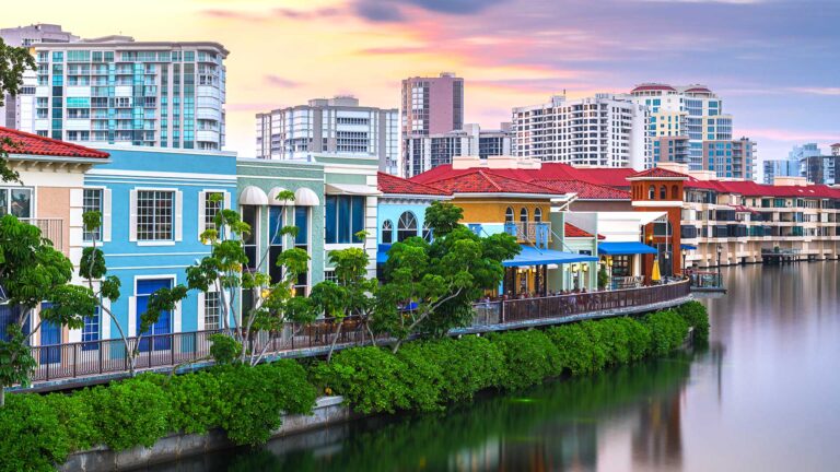 Colorful buildings line a waterfront at sunset, with tall modern skyscrapers in the background.