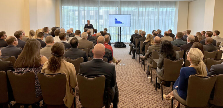 Audience listens to a speaker presenting a bar graph in a conference room.