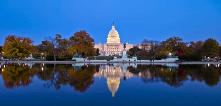 The U.S. Capitol building at dusk, with its reflection visible in the water of the Capitol Reflecting Pool.