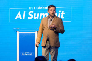 A person in a brown blazer speaks on stage at the BST Global AI Summit, with a blue background displaying the event name.