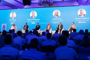 A panel of six people on stage discussing technology topics at a conference, with a large audience watching.