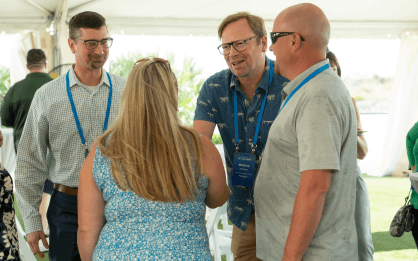 Four people engaged in conversation at an outdoor event with name badges and lanyards.