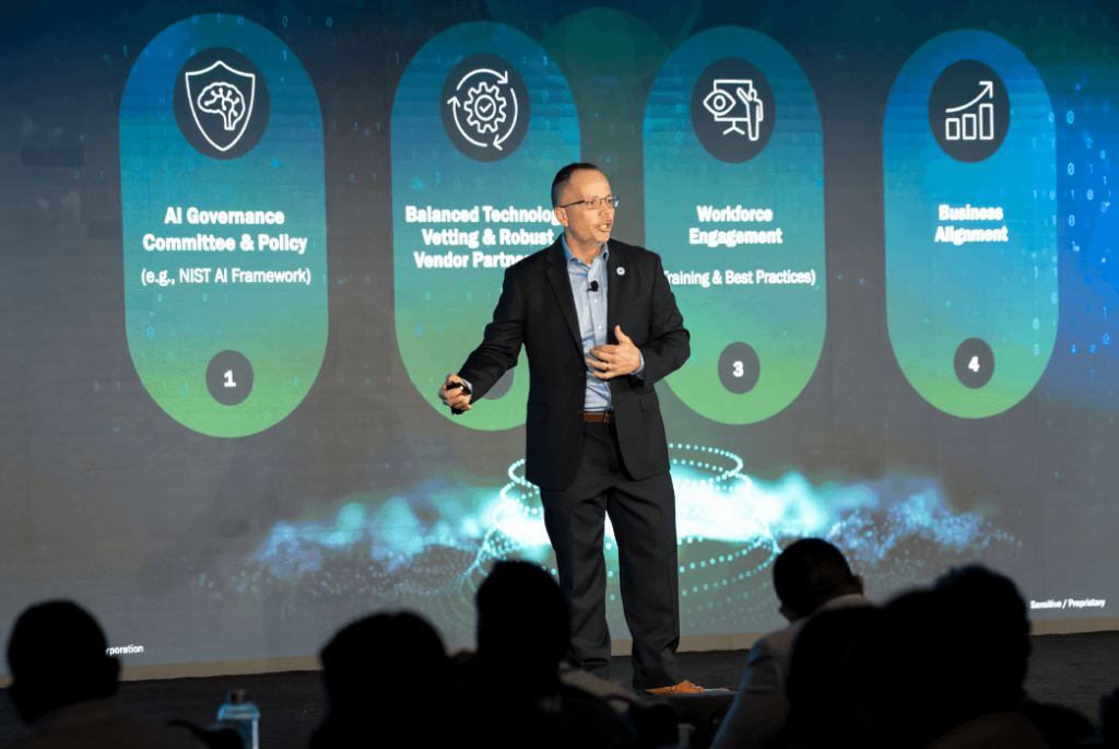 Ricardo Lorenzo in business attire presents on stage in front of a screen displaying four business-related topics with icons and brief descriptions.