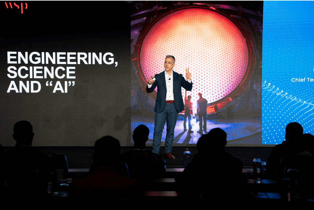 Chadi Habib in a suit speaks on stage at a conference, with "ENGINEERING, SCIENCE AND 'AI'" displayed on a large screen behind him.